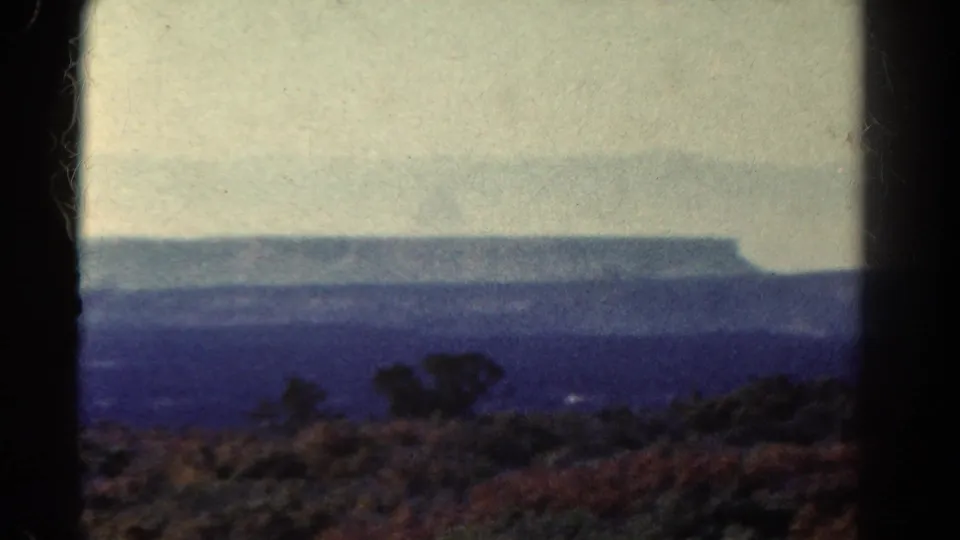 1967 Colorado frame with darker foreground brush, blue atmospheric haze, and a flat-topped plateau across the distance.