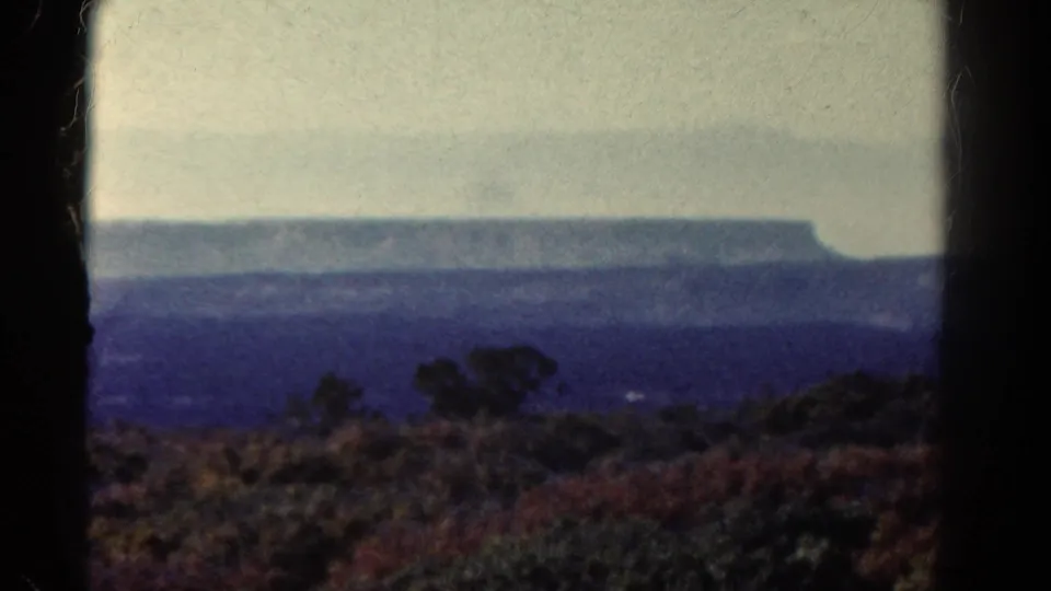 1967 Colorado 8mm frame showing a hazy flat-topped mountain and brushy foreground from a roadside viewpoint.