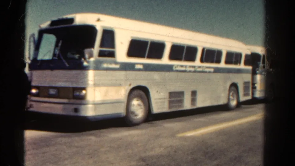 1967 Colorado 8mm frame showing a white-and-blue tour coach in side view on a sunlit asphalt road.
