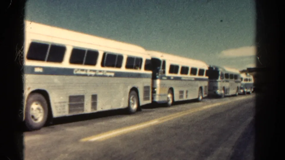1967 Colorado roadside frame showing several matching white-and-blue tour coaches lined up along the asphalt.