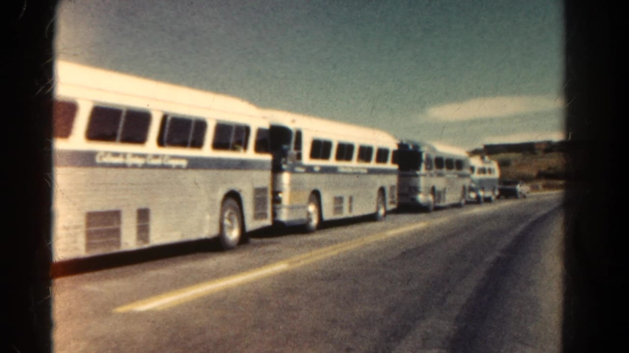 1967 Colorado 8mm frame showing several white and blue tour buses parked along a road, viewed through dark window or film borders.
