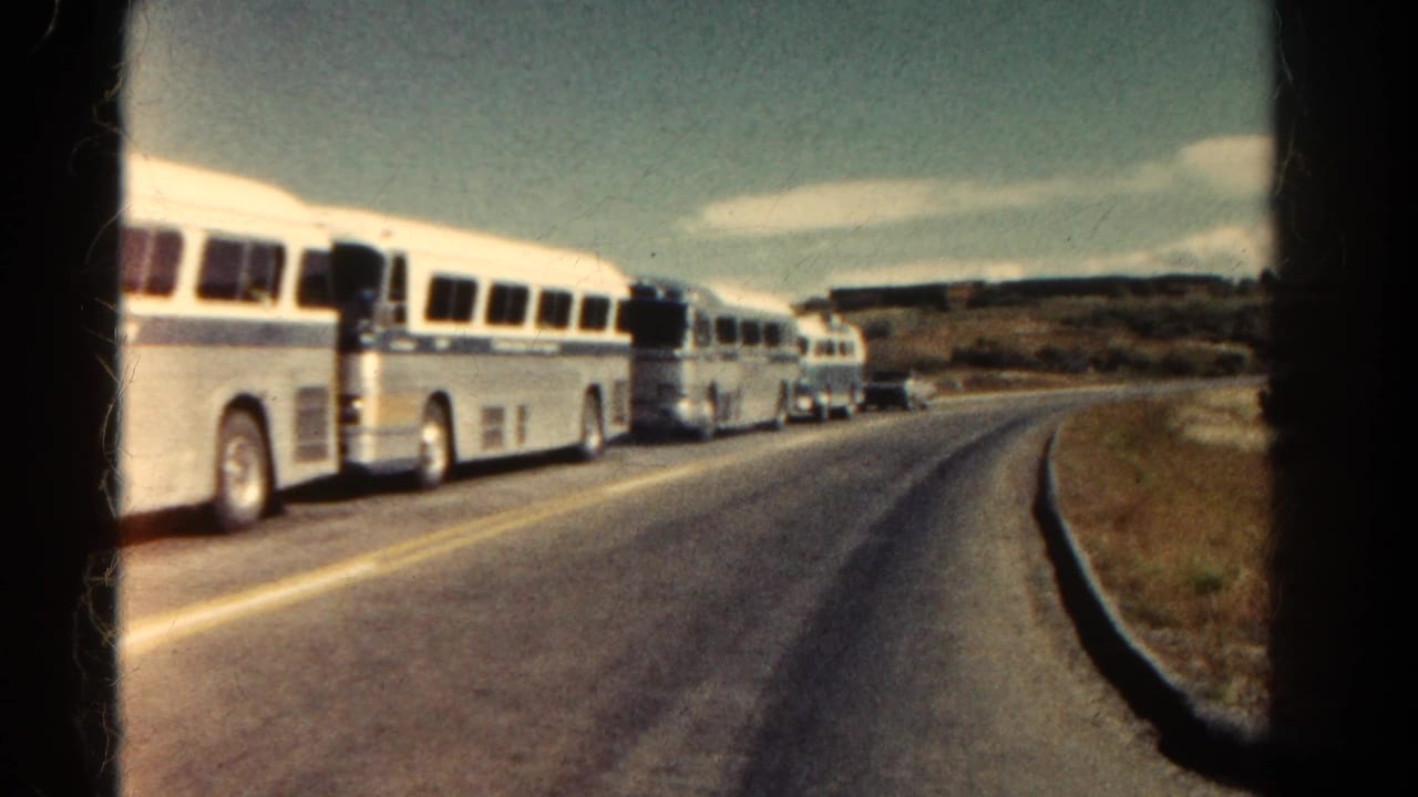 White and blue tour buses appear parked along a winding Colorado road in 1967, with dry grass and low hills beyond.