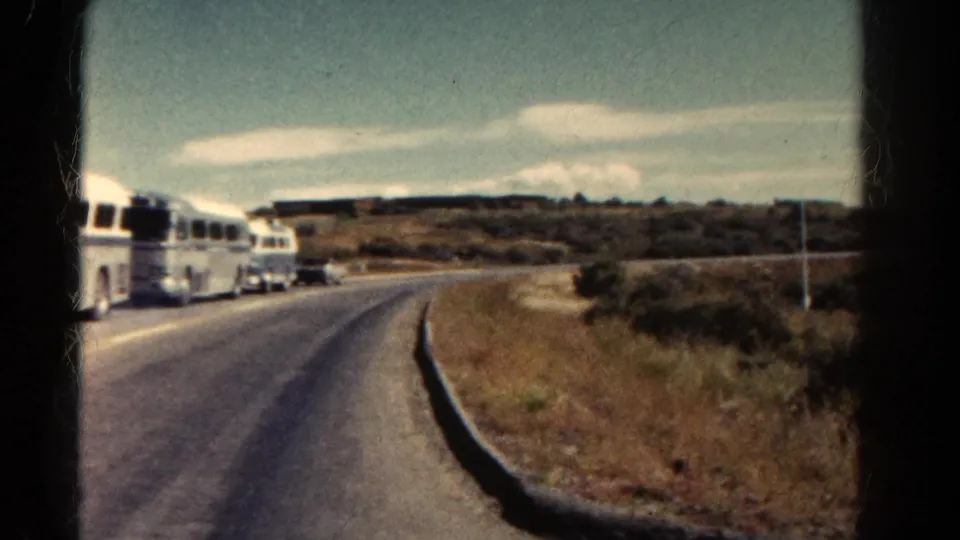 The final 1967 Colorado frame shows buses farther down the road, with the curve, shoulder, and open hillside more prominent.