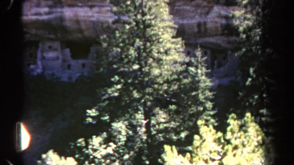 Colorado mountain ruin view on 8mm film, with pines and bright foliage partly hiding stone structures in shadow.