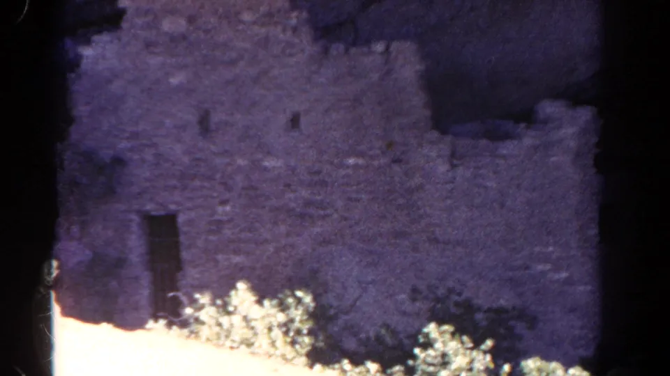 1967 Mesa Verde frame showing masonry wall details, small rectangular openings, and sunlit brush below.