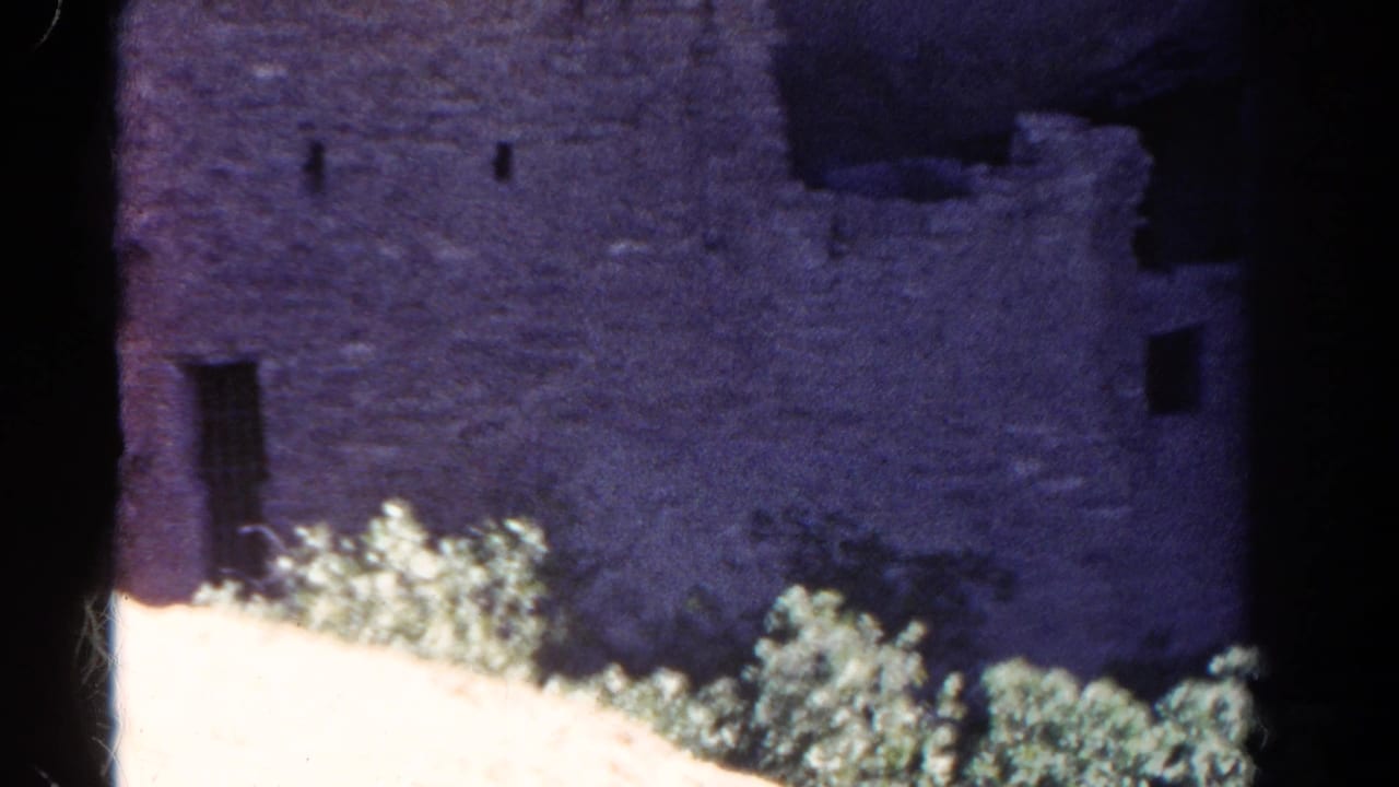 1967 Colorado 8mm frame showing a weathered stone structure with small openings, shrubs and dark scan borders.