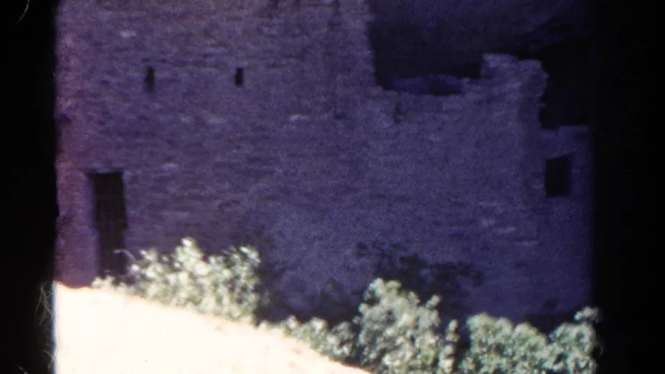 1967 Colorado 8mm frame showing a weathered stone structure with small openings, shrubs and dark scan borders.