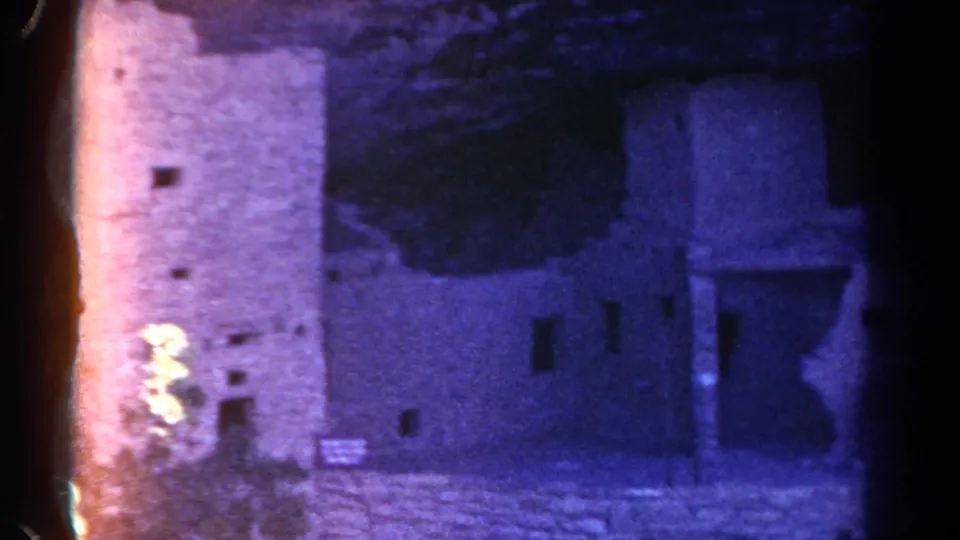 1967 Colorado 8mm frame showing stone building remains, a dark doorway, small sign and rocky ground.