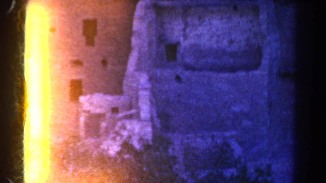 1967 Colorado 8mm frame of a weathered ruin facade partly obscured by a vertical orange light leak and blue-purple color shift.