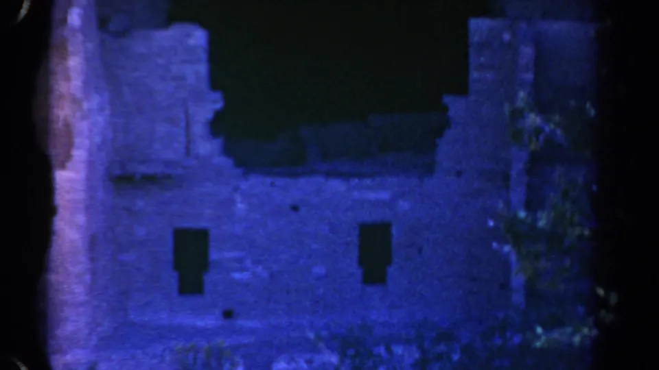 1967 Colorado 8mm frame of a blue-tinted ruin wall with dark roofline shadow, small window openings, and vegetation along the right edge.