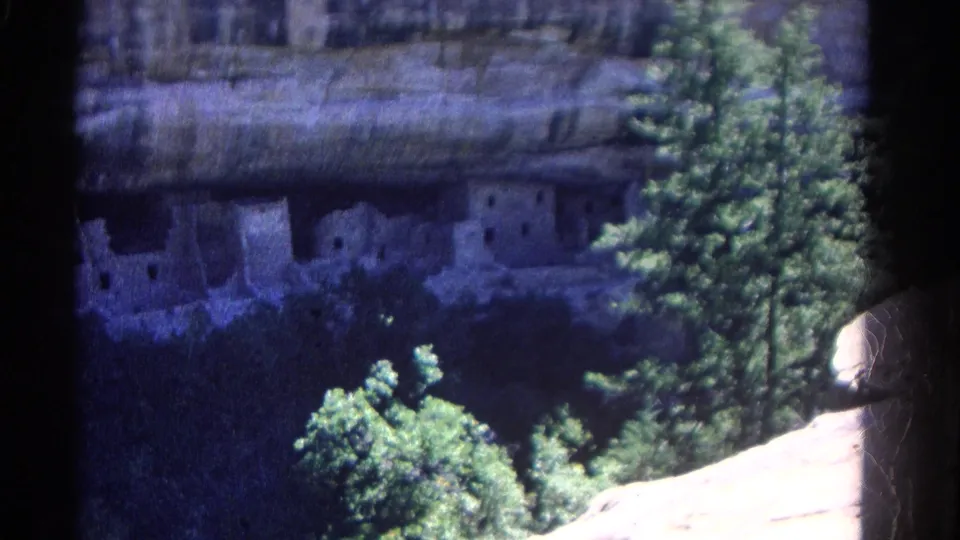 1967 Colorado 8mm still of cliff dwellings below a broad rock overhang, seen from an elevated visitor vantage point.