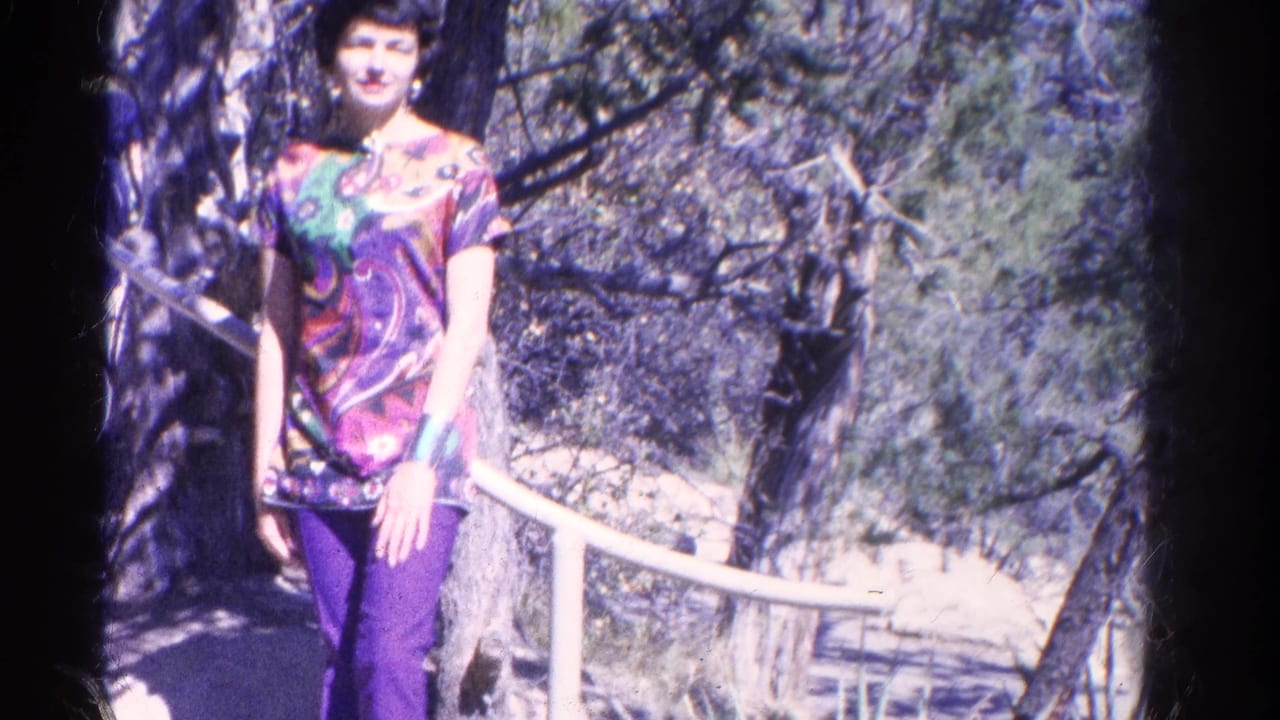 Woman in purple pants and patterned top stands beside a white railing on a wooded trail.