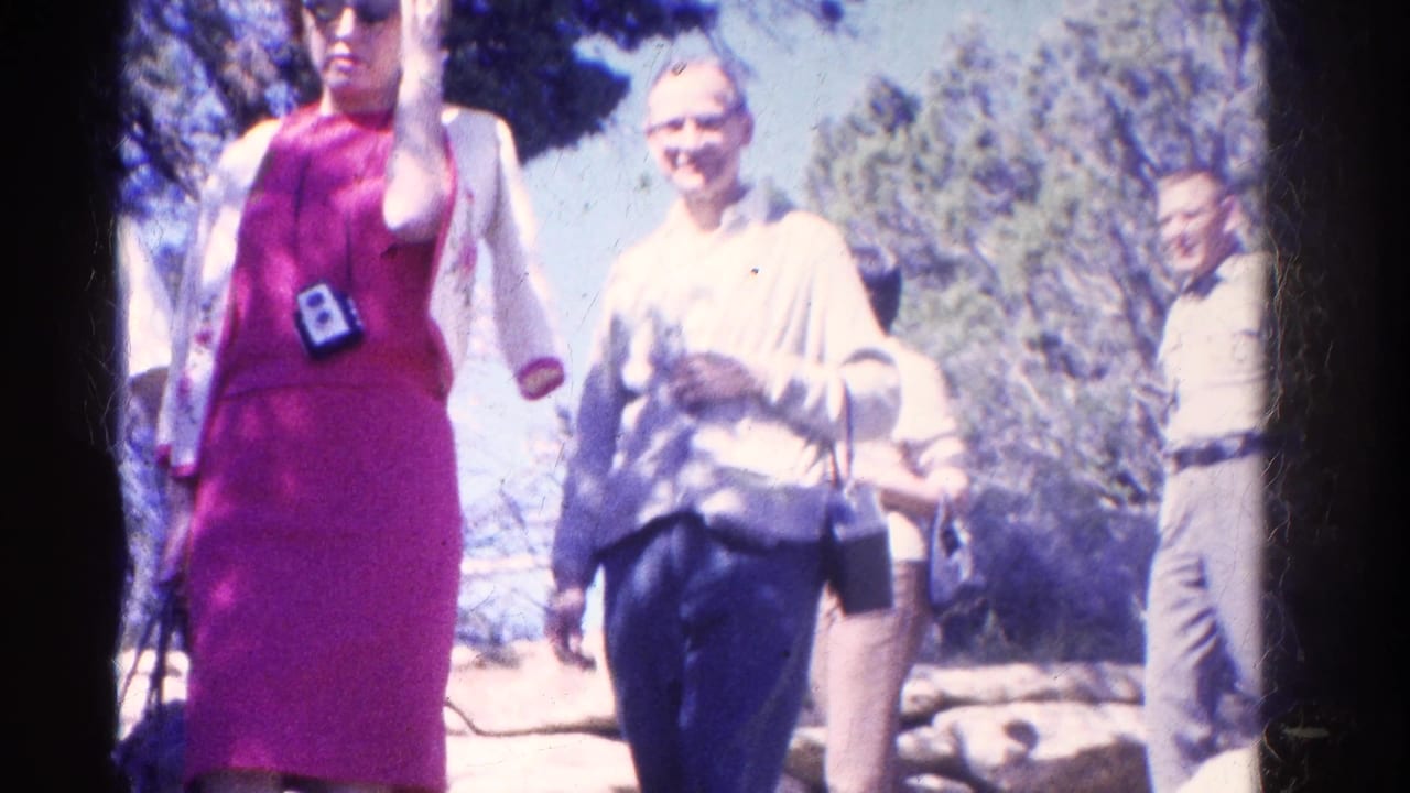 Two women walk toward the camera while other adults stand along a wooded trail.