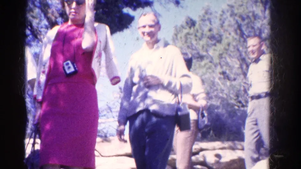 A woman in a pink dress and an older woman in a light blouse walk toward the camera on a sunlit Colorado trail in 1967.
