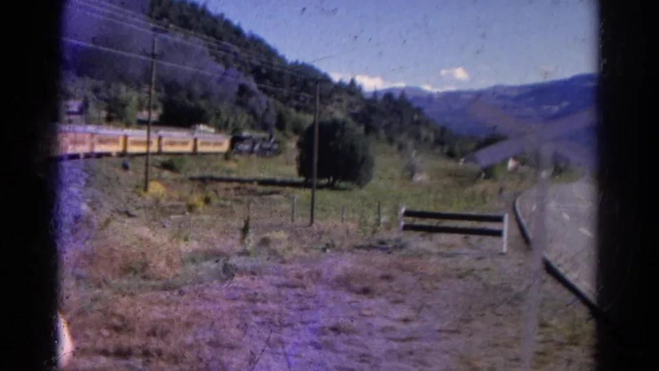 1967 Colorado 8mm frame showing yellow rail cars in a mountain valley beside a rural road and utility pole.