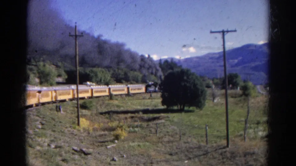 1967 Colorado home-movie frame showing yellow rail cars moving through open countryside under a clear mountain sky.