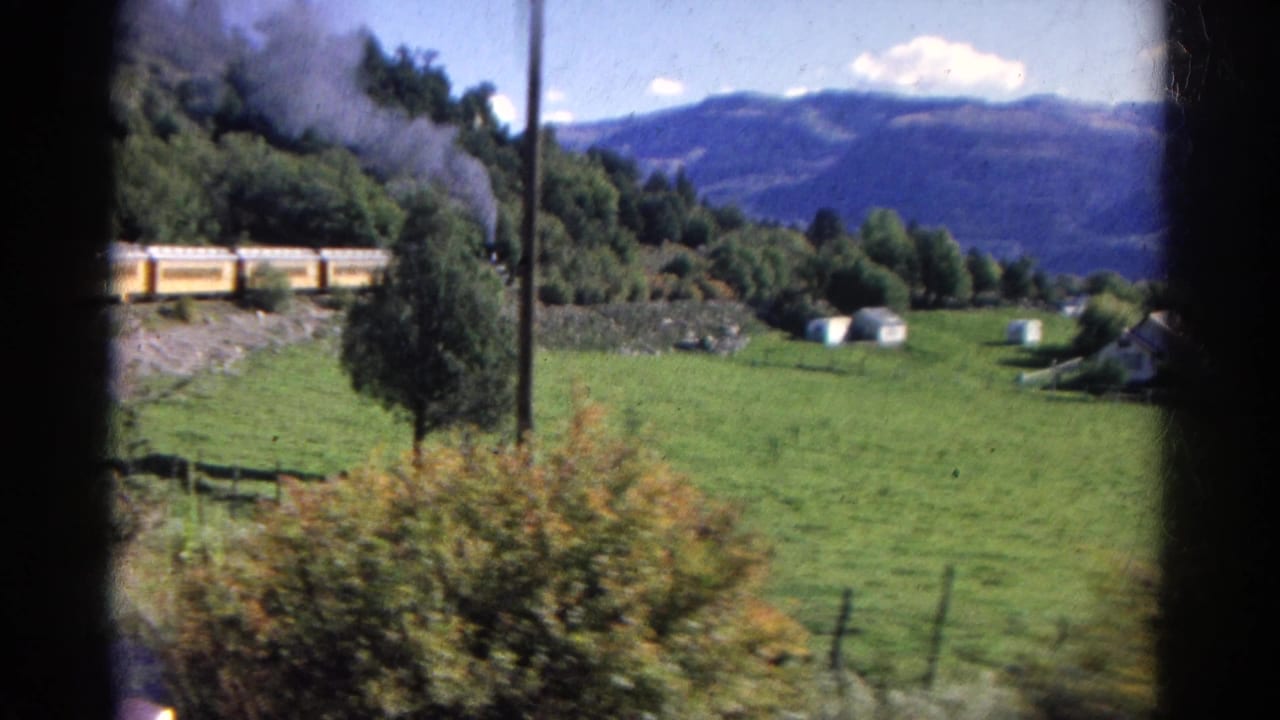 1967 Colorado 8mm frame showing a steam train with yellow passenger cars moving past fields, trees, and distant mountains.