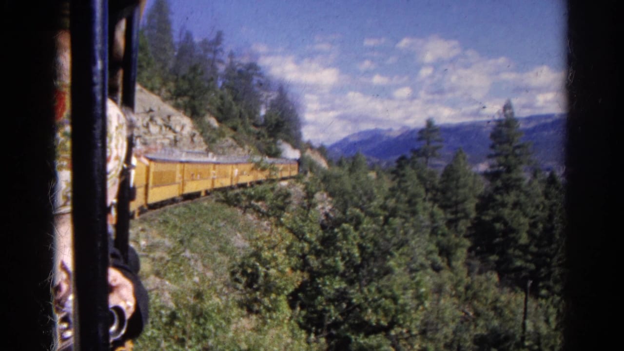 Yellow train beside a rocky slope, seen from a passenger window with a partial person at edge.