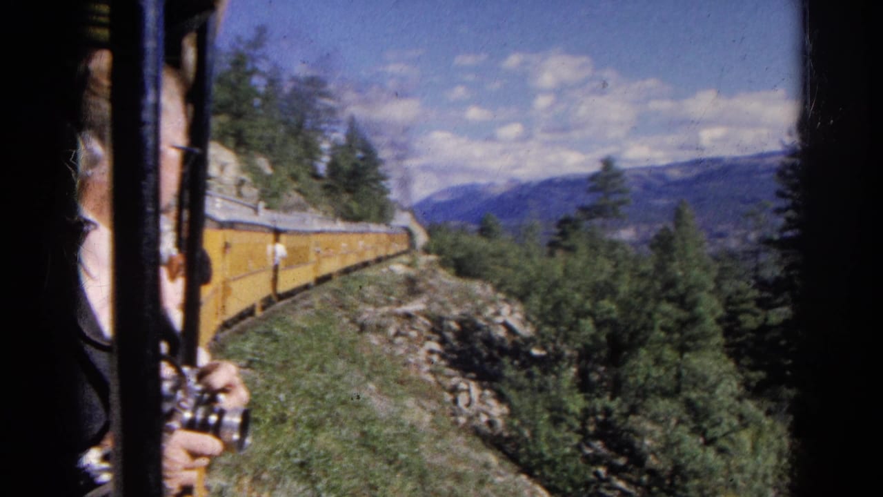 Passenger with camera beside a yellow train on a mountain route.