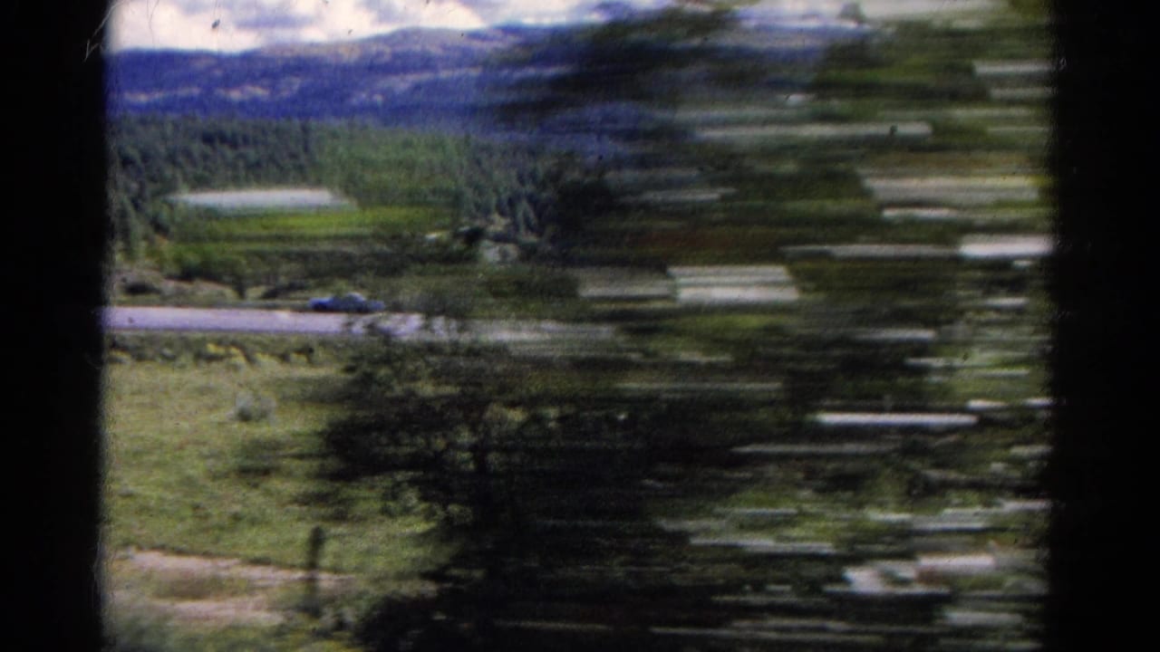Blurred view from train window toward road, trees, and mountains.