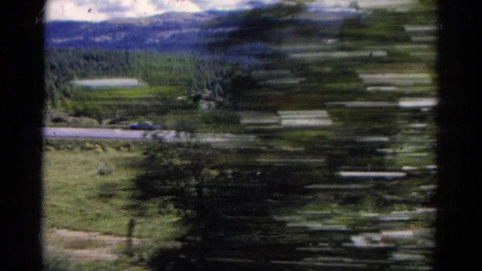 View from the moving Colorado train across trees, highway, grassy land, and distant mountains with strong motion blur.