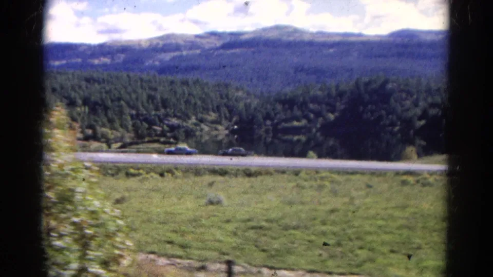 Colorado mountain landscape seen from the train, with a car on the highway below and forested slopes in the distance.