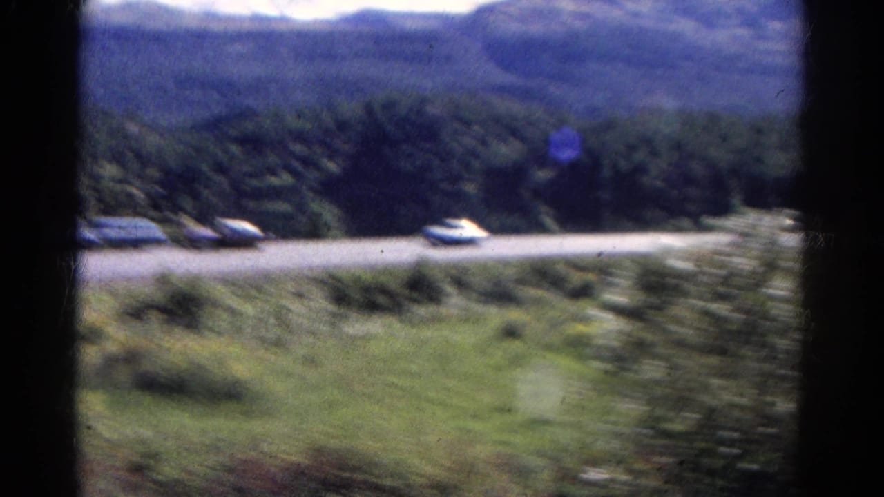 Blurred roadside view with cars on a road below green hills.