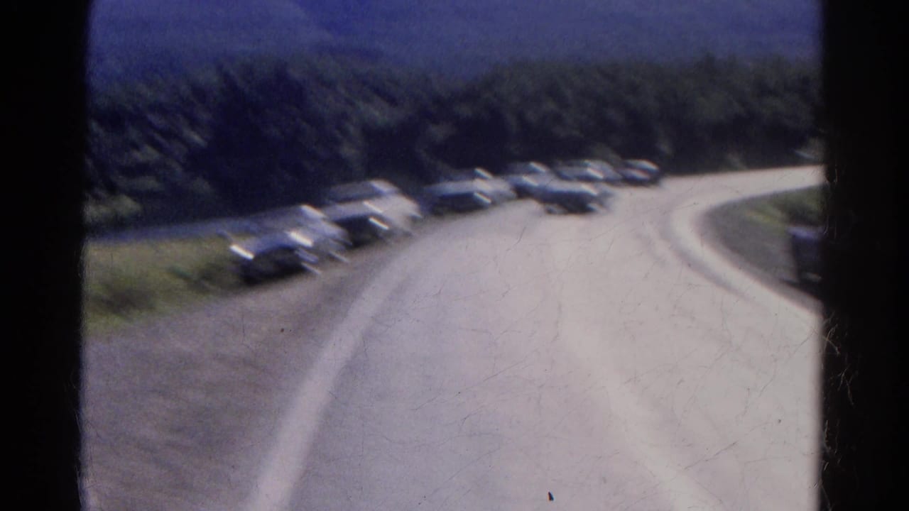 Blurred train view of cars lined along a curving mountain road.