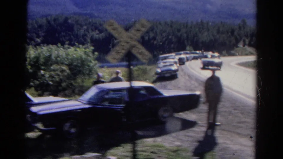 1967 Colorado roadside scene with cars stopped near a railroad crossing sign as people stand watching the passing train.