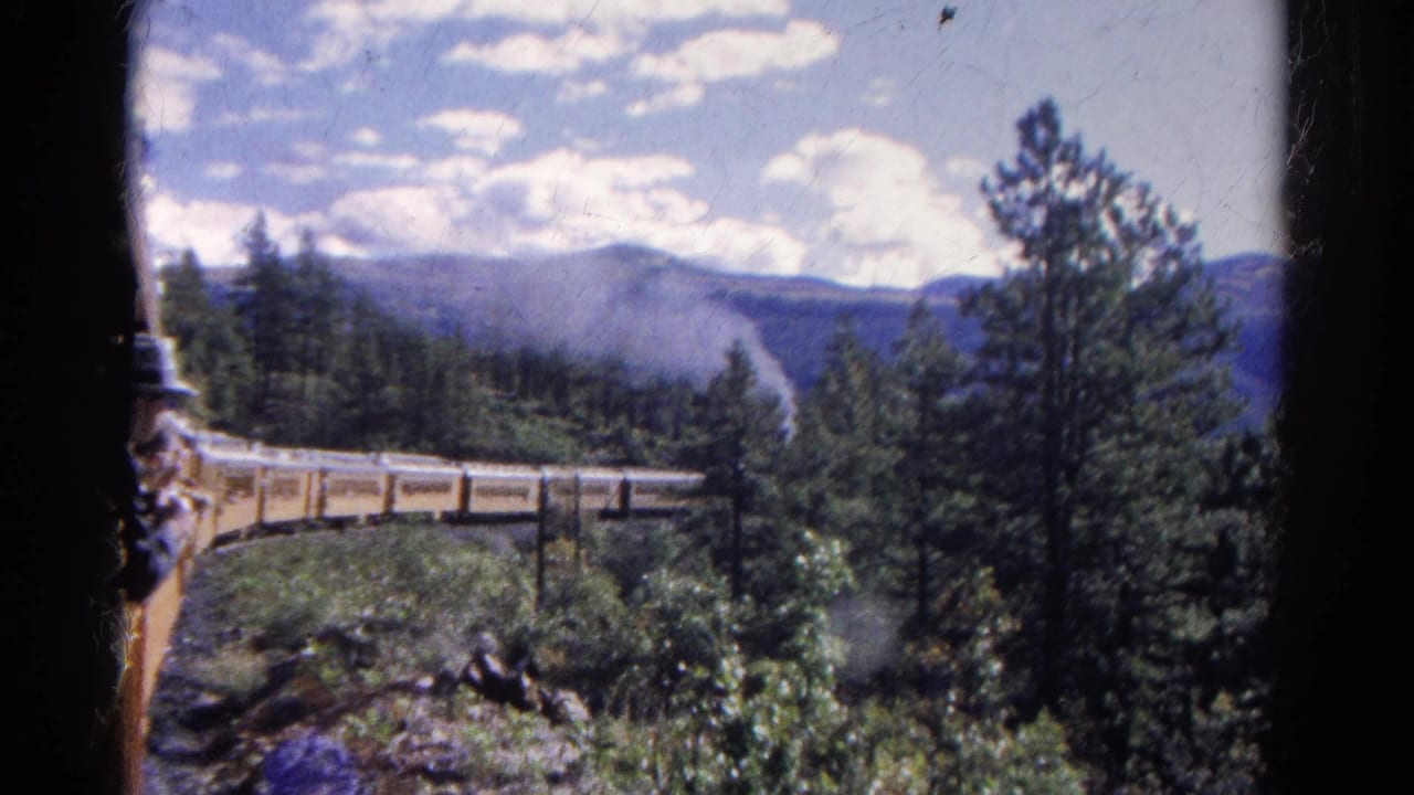 1967 Colorado 8mm frame showing a passenger at a train window with a train, bridge, pine trees, and distant mountains beyond.