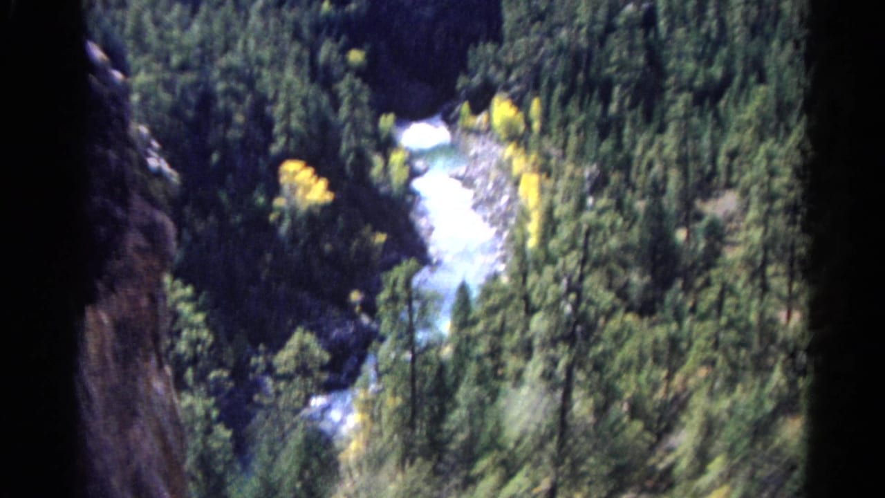 River canyon seen through dark film borders with forested slopes and bright autumn foliage.