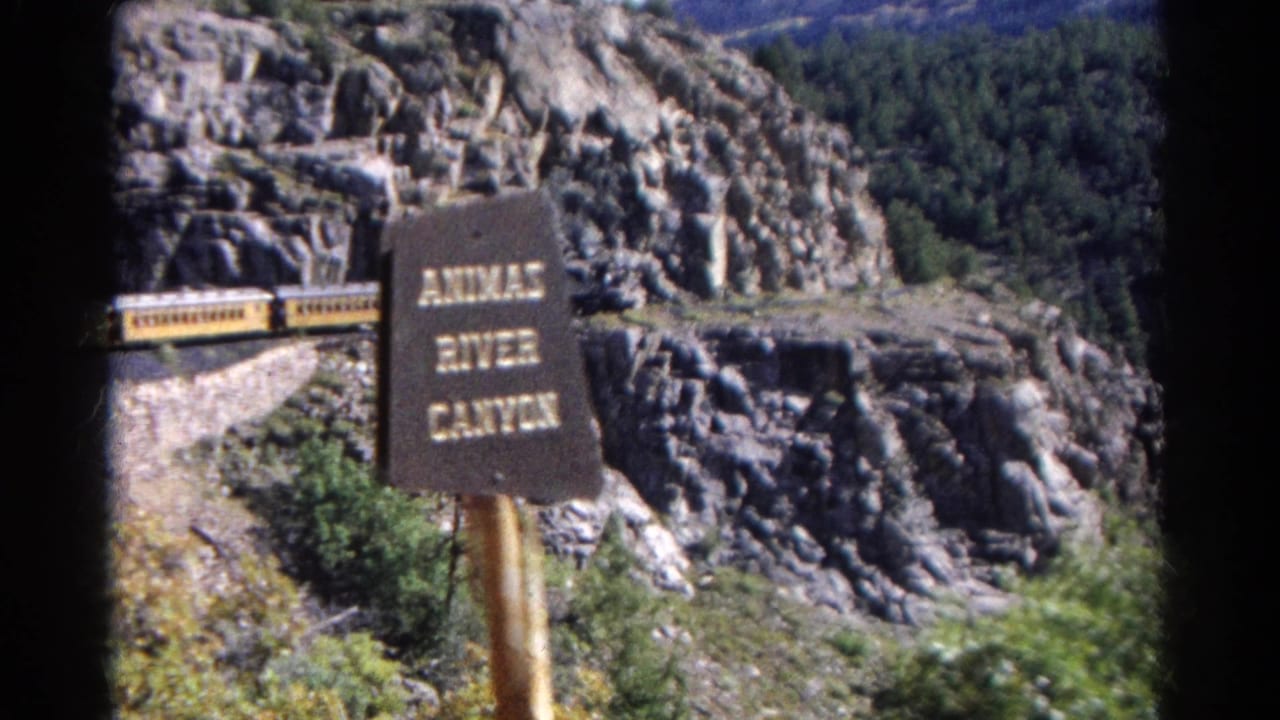 Yellow passenger train beside a rocky cliff with an Animas River Canyon sign in front.