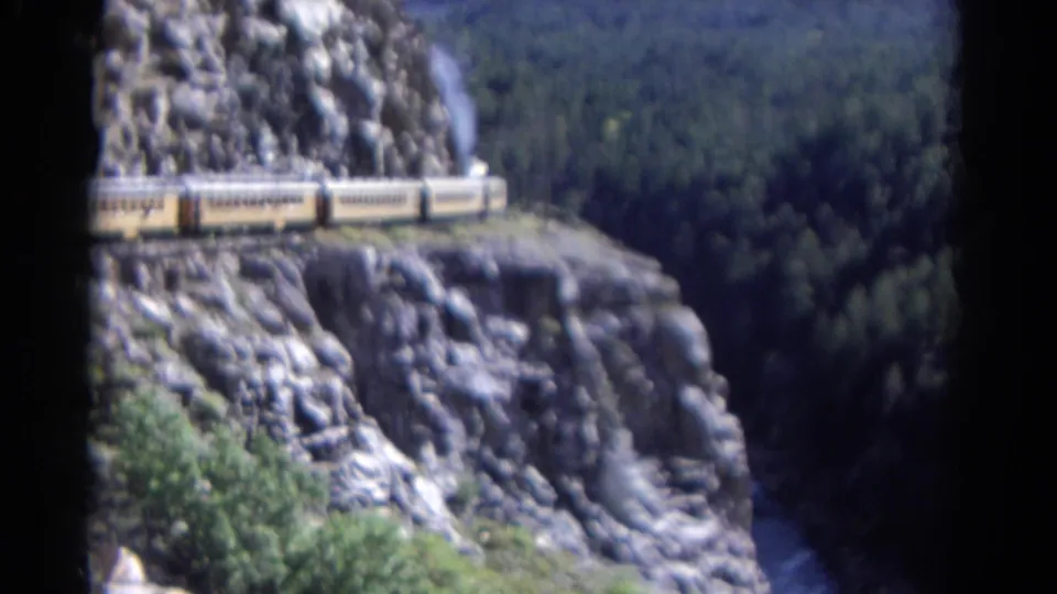 1967 Colorado 8mm frame showing the rear passenger cars of a steam train on a cliffside route above a wooded valley.