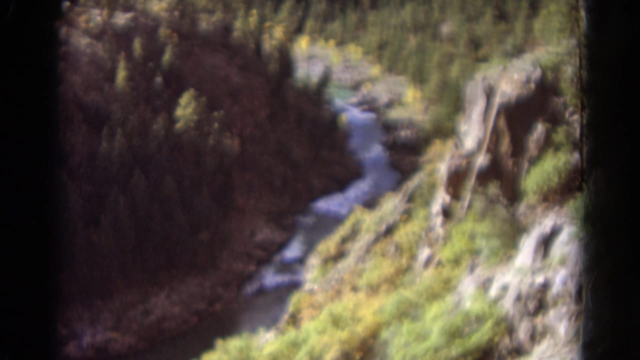 1967 Colorado home-movie frame of flowing water cutting through a wooded canyon with rocky outcrops.