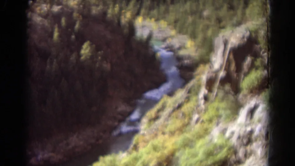 1967 Colorado home-movie frame of flowing water cutting through a wooded canyon with rocky outcrops.