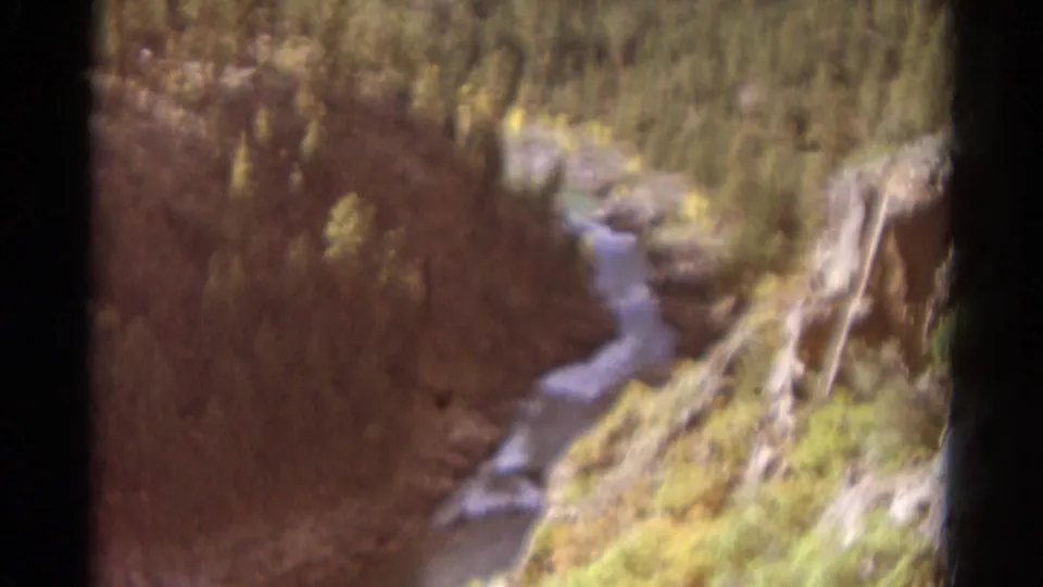 Vintage 8mm Colorado canyon view with a winding stream, autumn-toned brush, and rocky hillside.