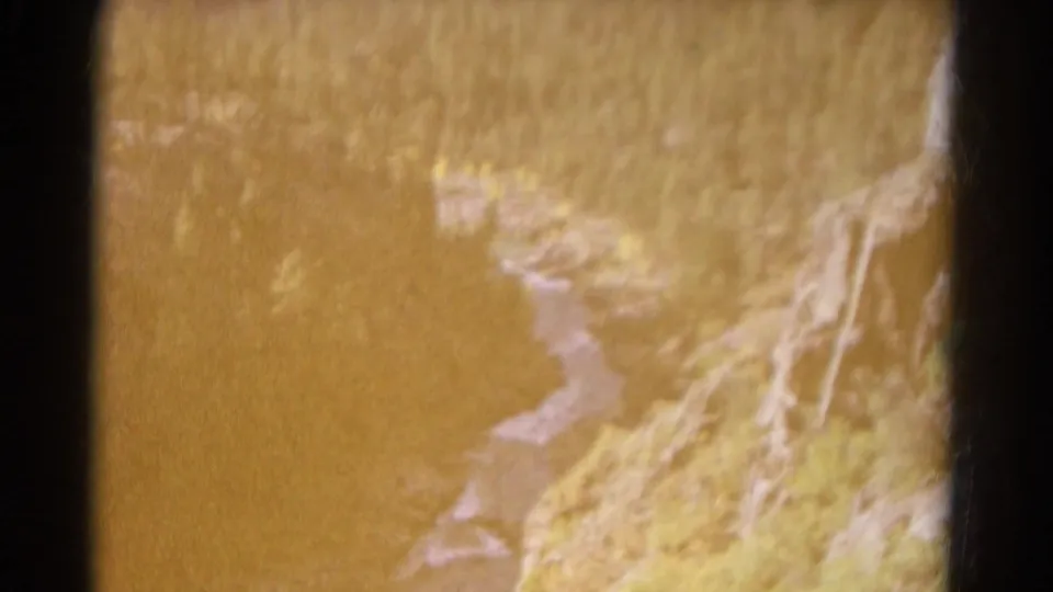 Warm, overexposed 1967 Colorado 8mm frame showing a pale stream beside a rocky, grassy canyon slope.