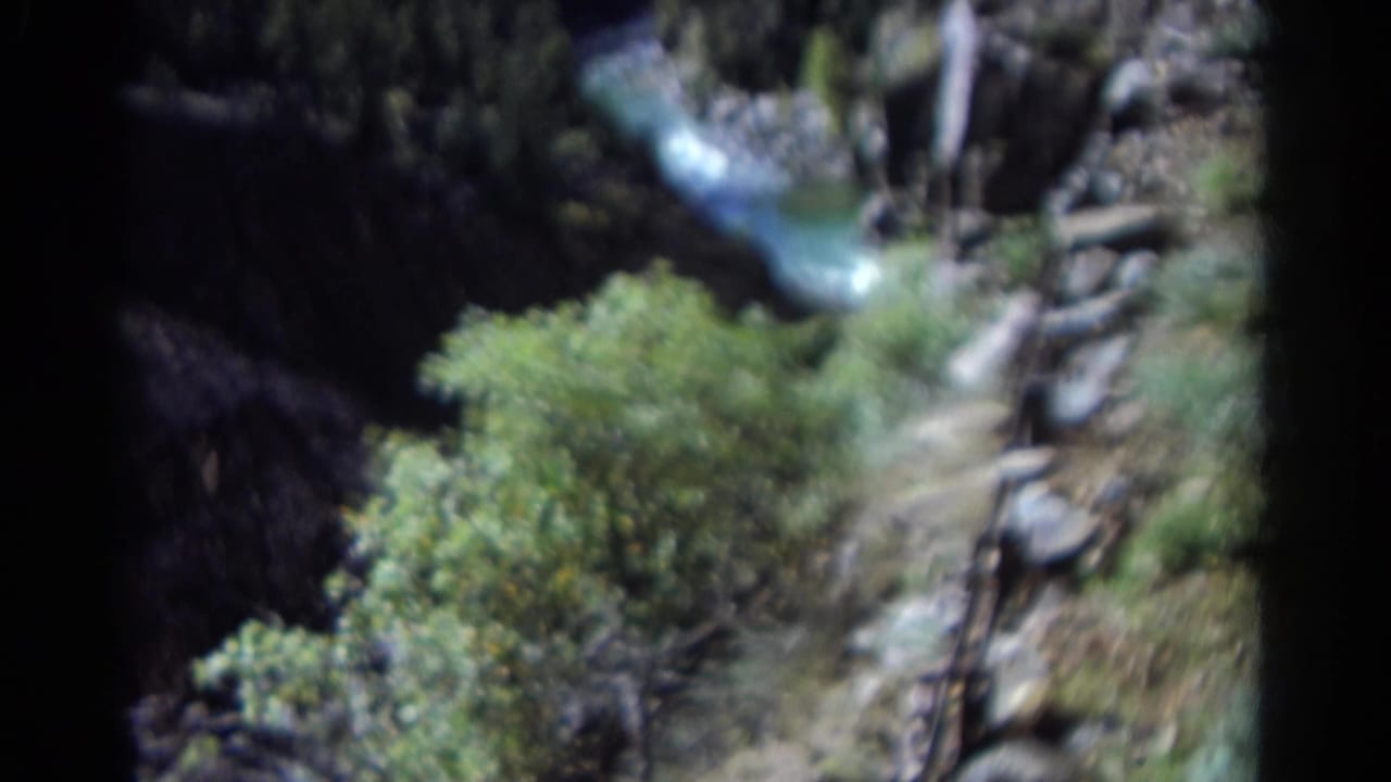 1967 Colorado 8mm view of a blue river below a rocky, forested canyon edge with dark projection borders.