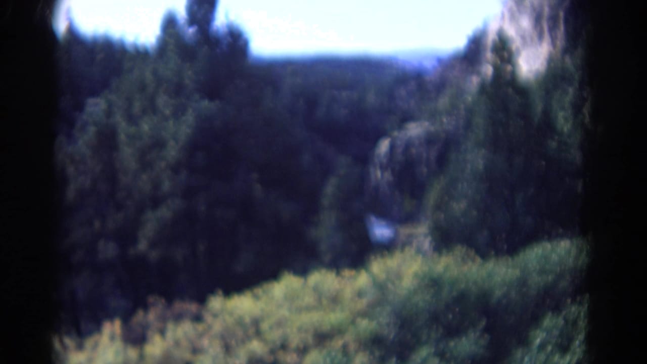 Forested mountain valley with rocky slopes and distant hills.