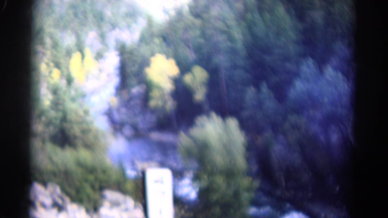 1967 Colorado home-movie frame showing a river corridor through trees, rocks, and yellow foliage in a mountain canyon.