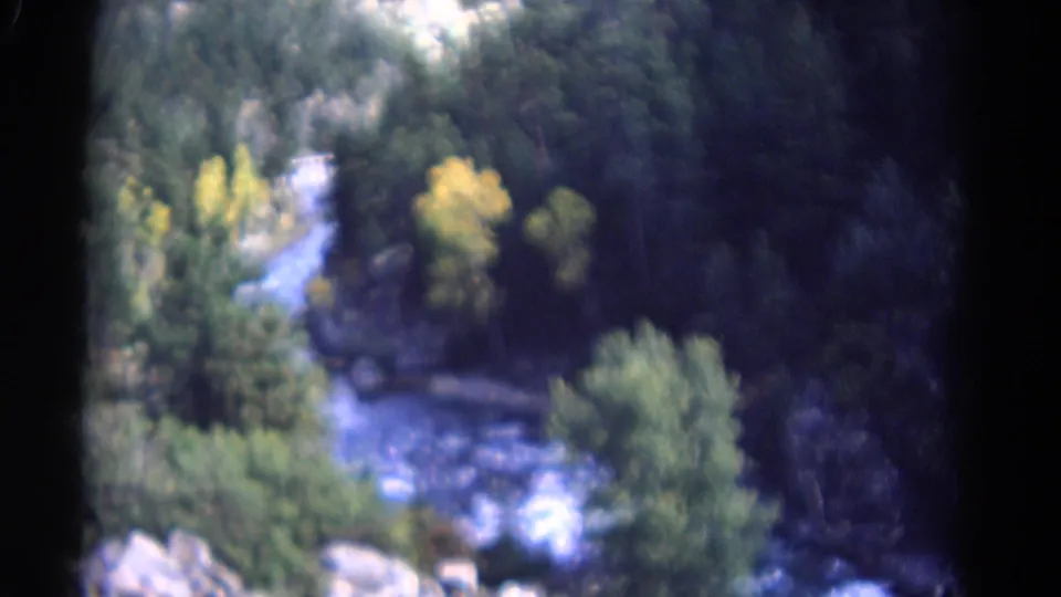 Elevated 1967 Colorado 8mm view of river rapids bordered by rocks, green trees, and yellow foliage.