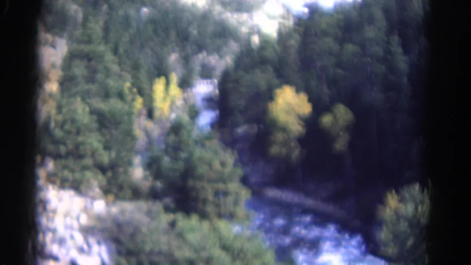 Soft 8mm Colorado aerial view of a river bend passing through dark forest with small patches of yellow autumn foliage.