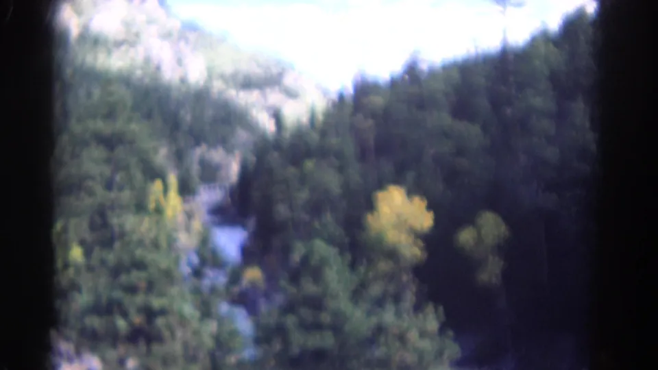 Aerial 8mm frame from Colorado showing a river, forested valley walls, distant hills, and yellow autumn trees.