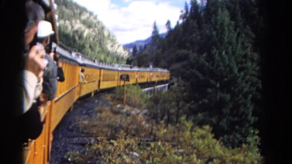 1967 Colorado home-movie view from inside a train, looking along yellow cars curving through a forested mountain valley.