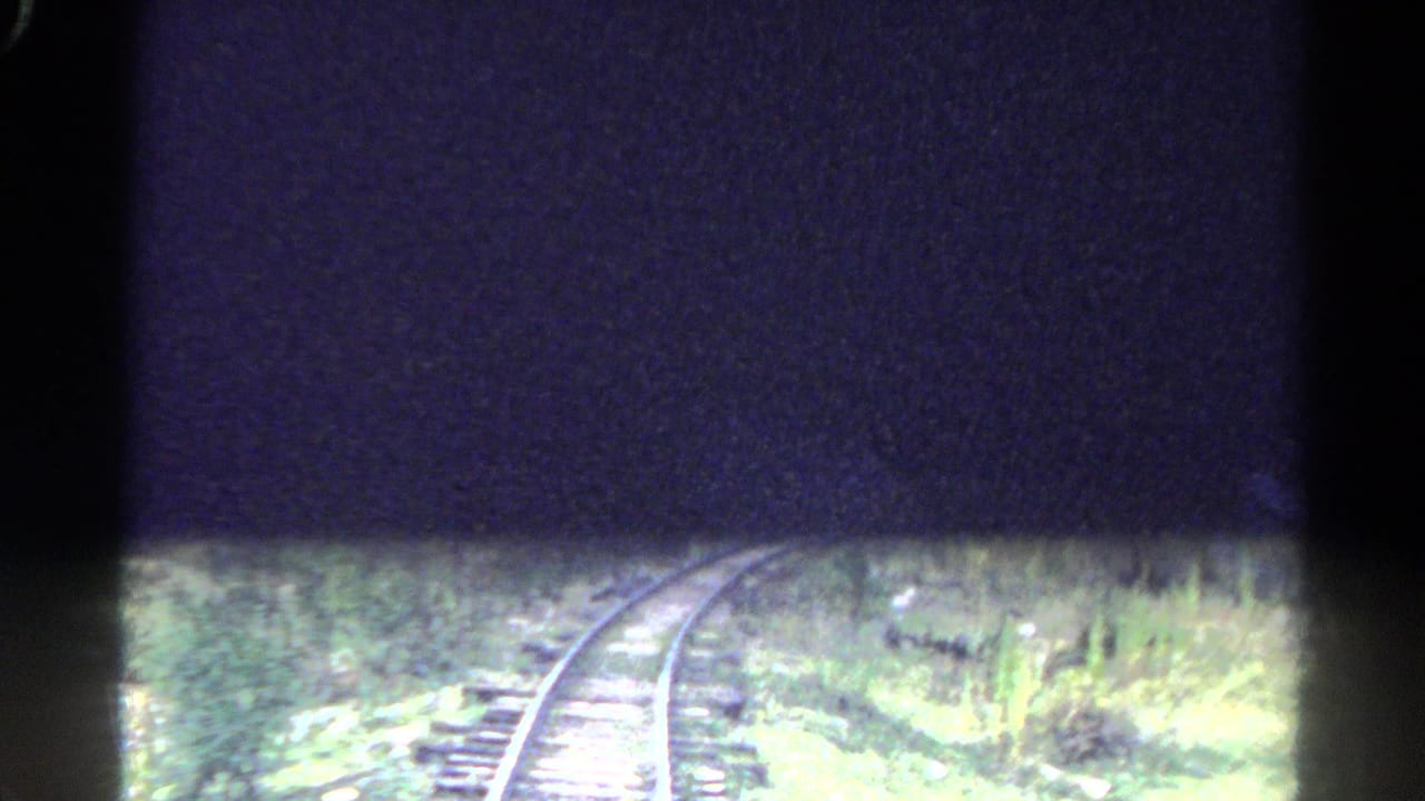 Curving railroad tracks run through green Colorado mountain vegetation, partly obscured by heavy 8mm frame shadowing.