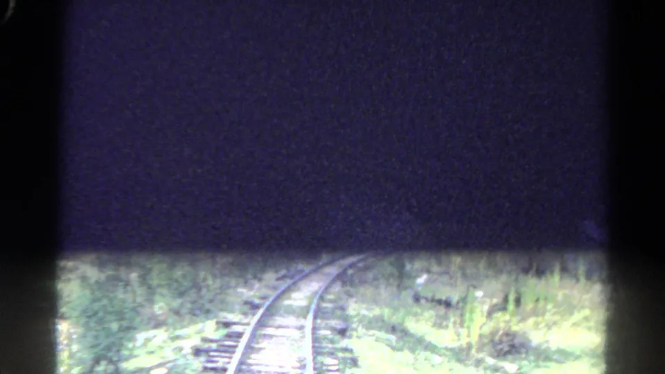 Curving railroad tracks run through green Colorado mountain vegetation, partly obscured by heavy 8mm frame shadowing.