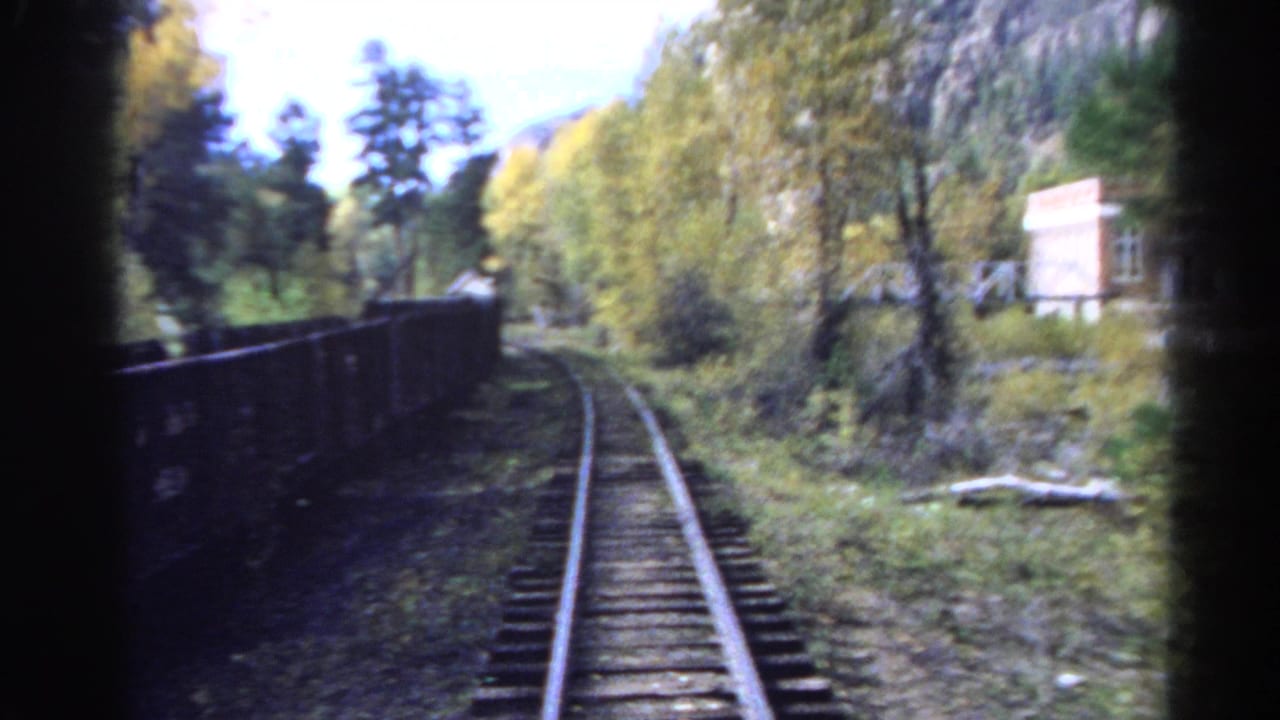 Railroad tracks curve through trees beside a mountain river corridor.