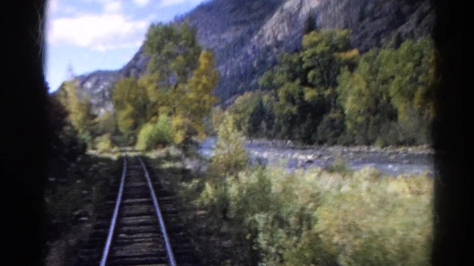 1967 Colorado 8mm still with a curving track, riverbank vegetation, autumn trees, and rugged mountainsides in the background.