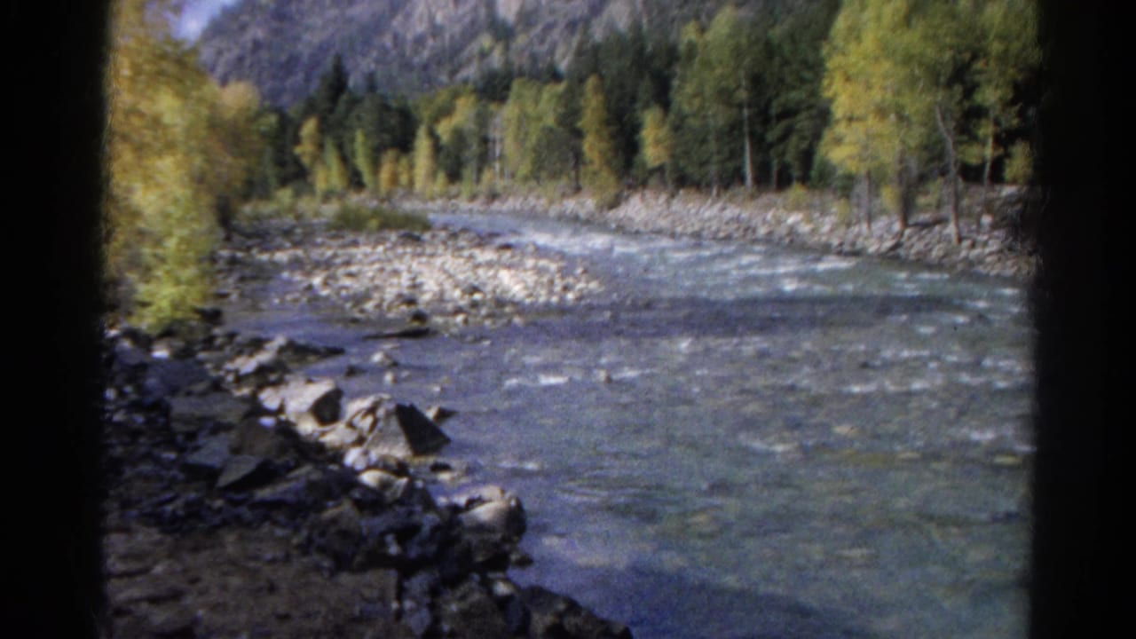 River curving through a wooded mountain valley beside rocky banks and train tracks.