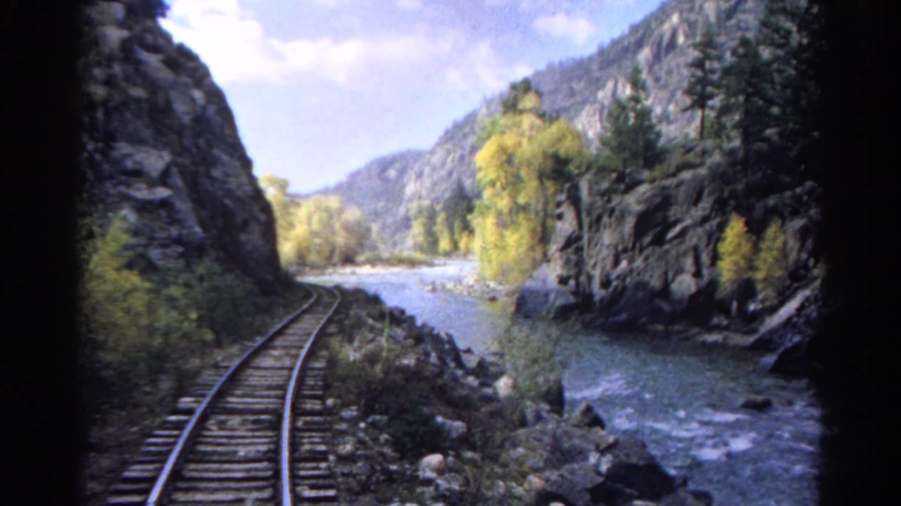 Curving railroad track beside a river in a rocky mountain canyon.